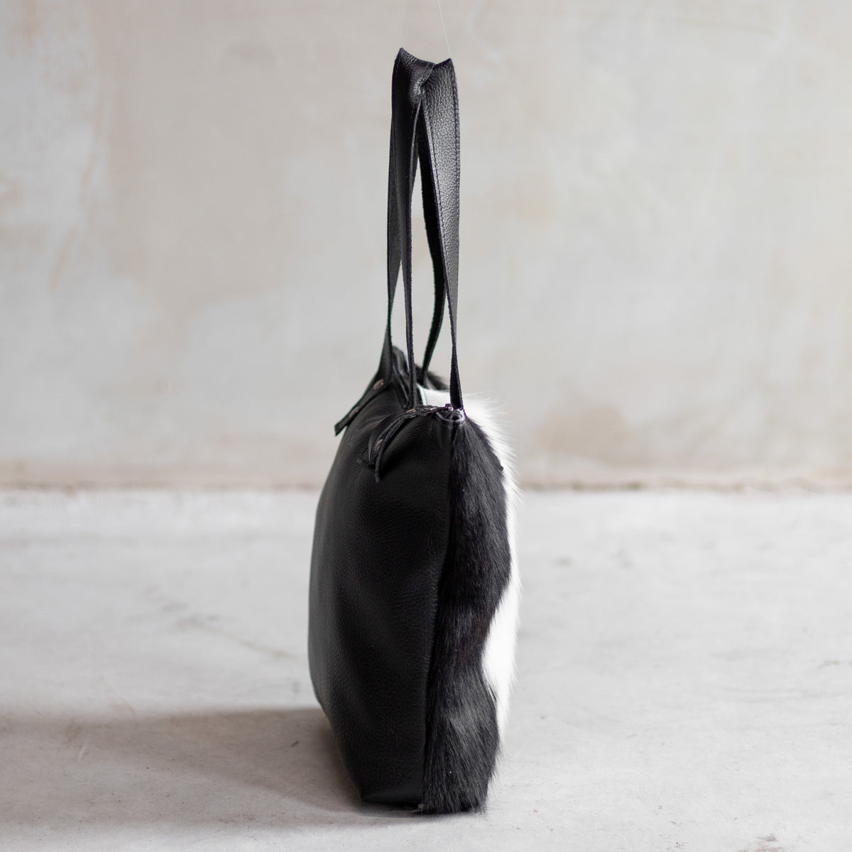 Sac à main épaule zippé en cuir et peau de vache noir et blanc, vu de profil