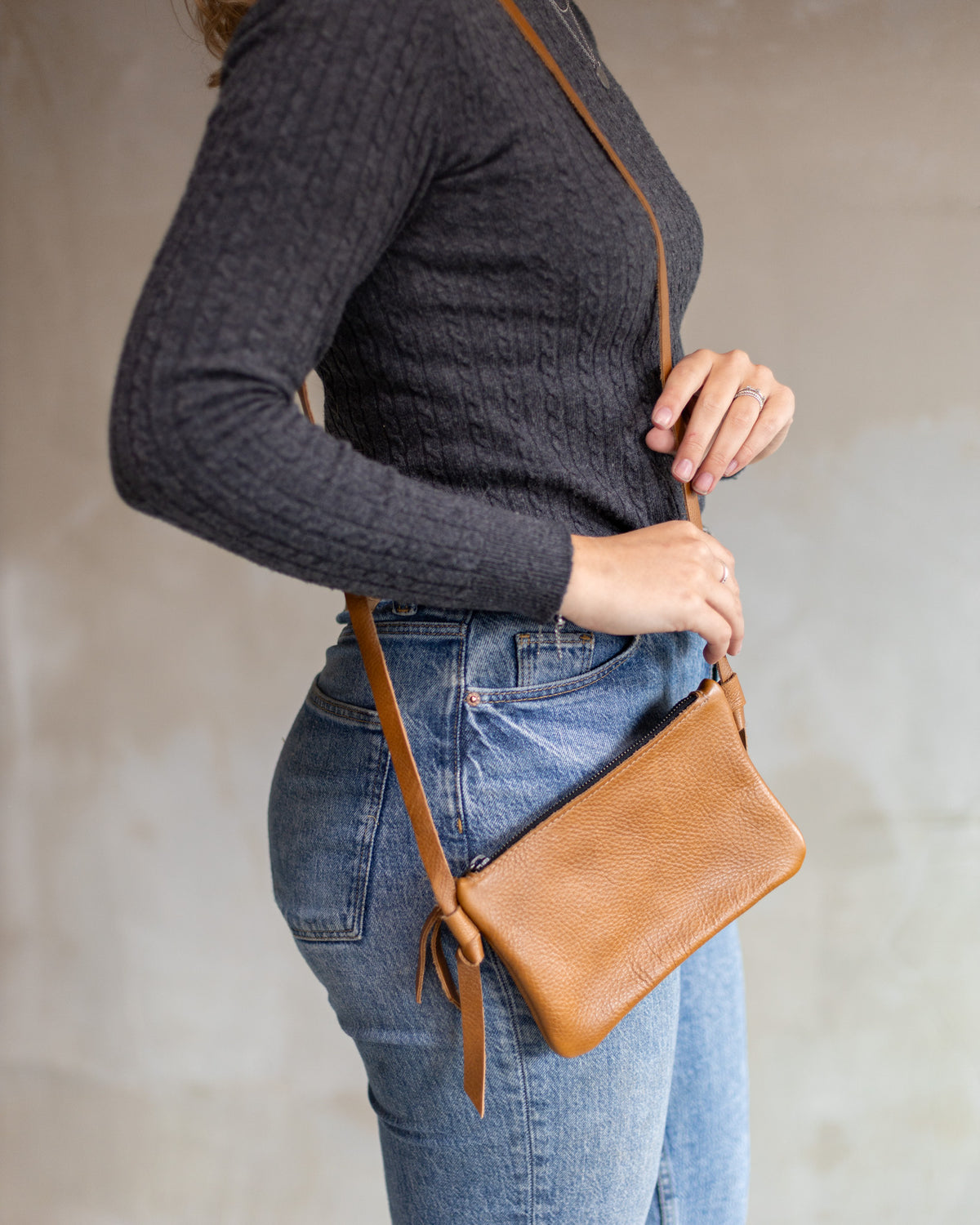 Sac à main pochette bandoulière en cuir cognac, portée en bandoulière avec un jean