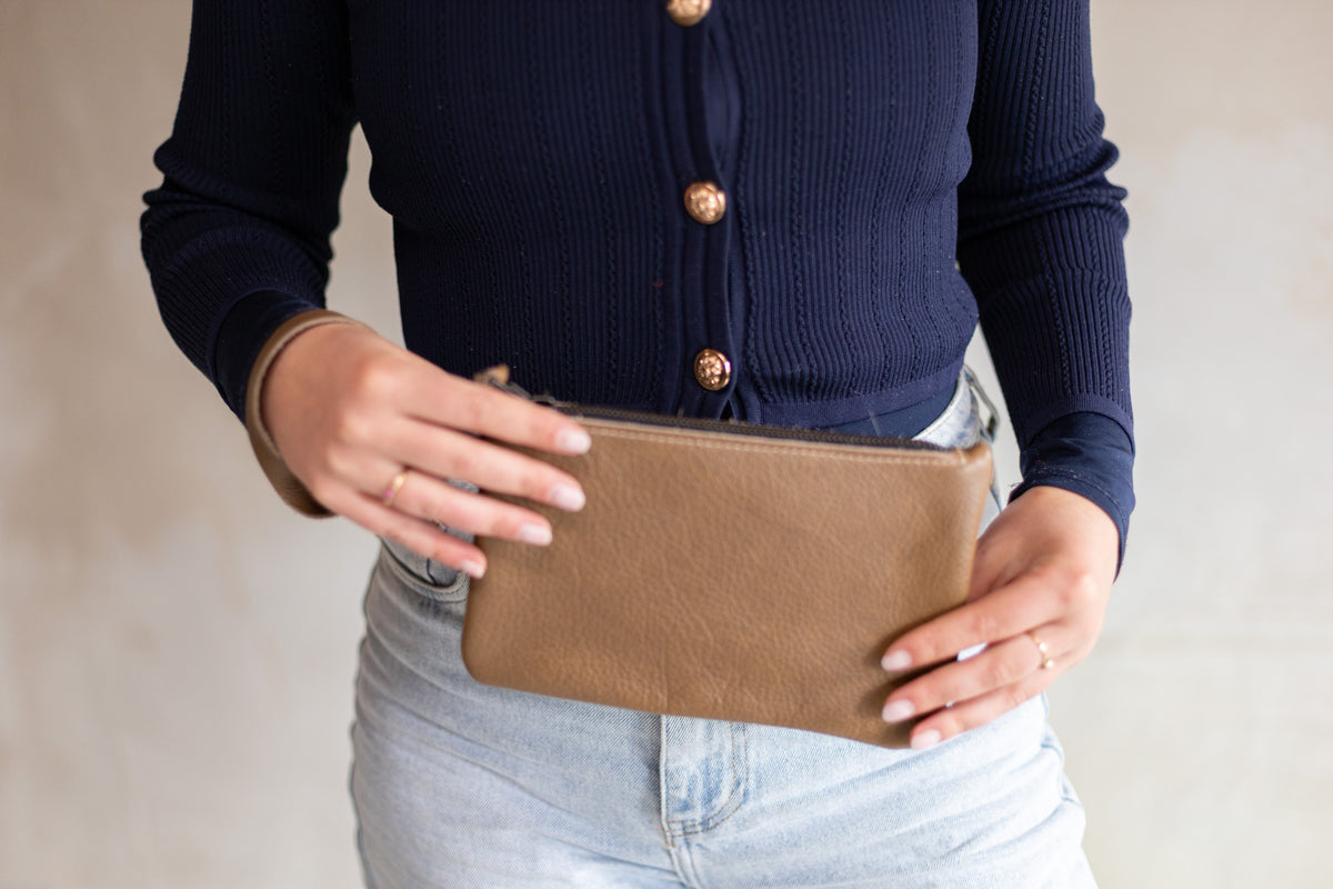Sac à main pochette en cuir sable, tenue à deux mains avec un jean