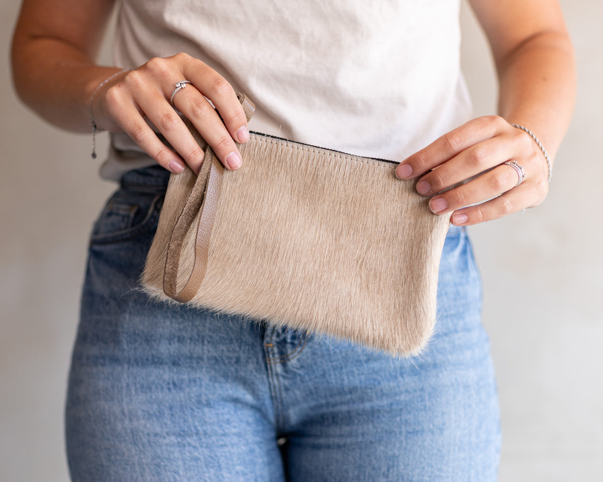 Sac à main pochette en peau de vache crème, tenue à deux mains avec un jean