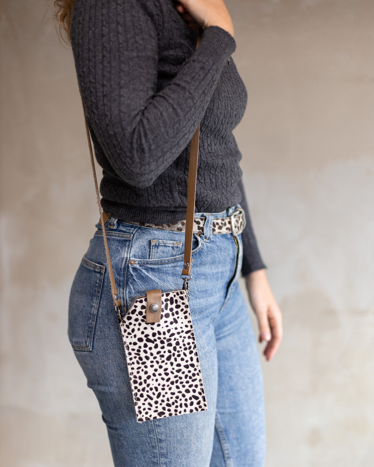 Sac à main pochette téléphone en peau de vache mini dalmatien, portée en bandoulière avec un jean