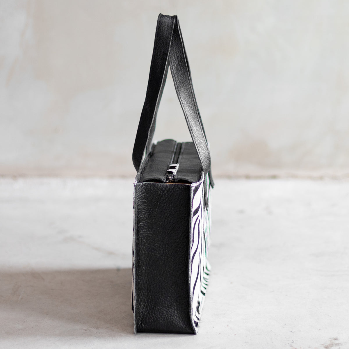 Sac à main rectangulaire en cuir noir et peau de vache zèbre, vu de profil