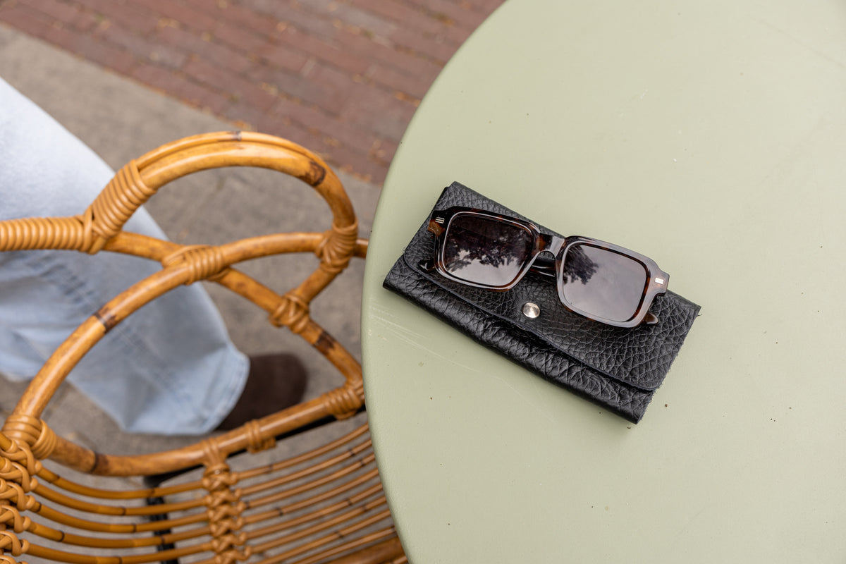 Étui à lunettes aimanté en cuir noir, étui posé dans un panier en osier avec des lunettes