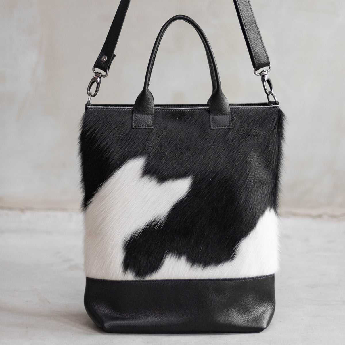 Grand sac à main en cuir et peau de vache noir et blanc, vu de face avec anses et bandoulière