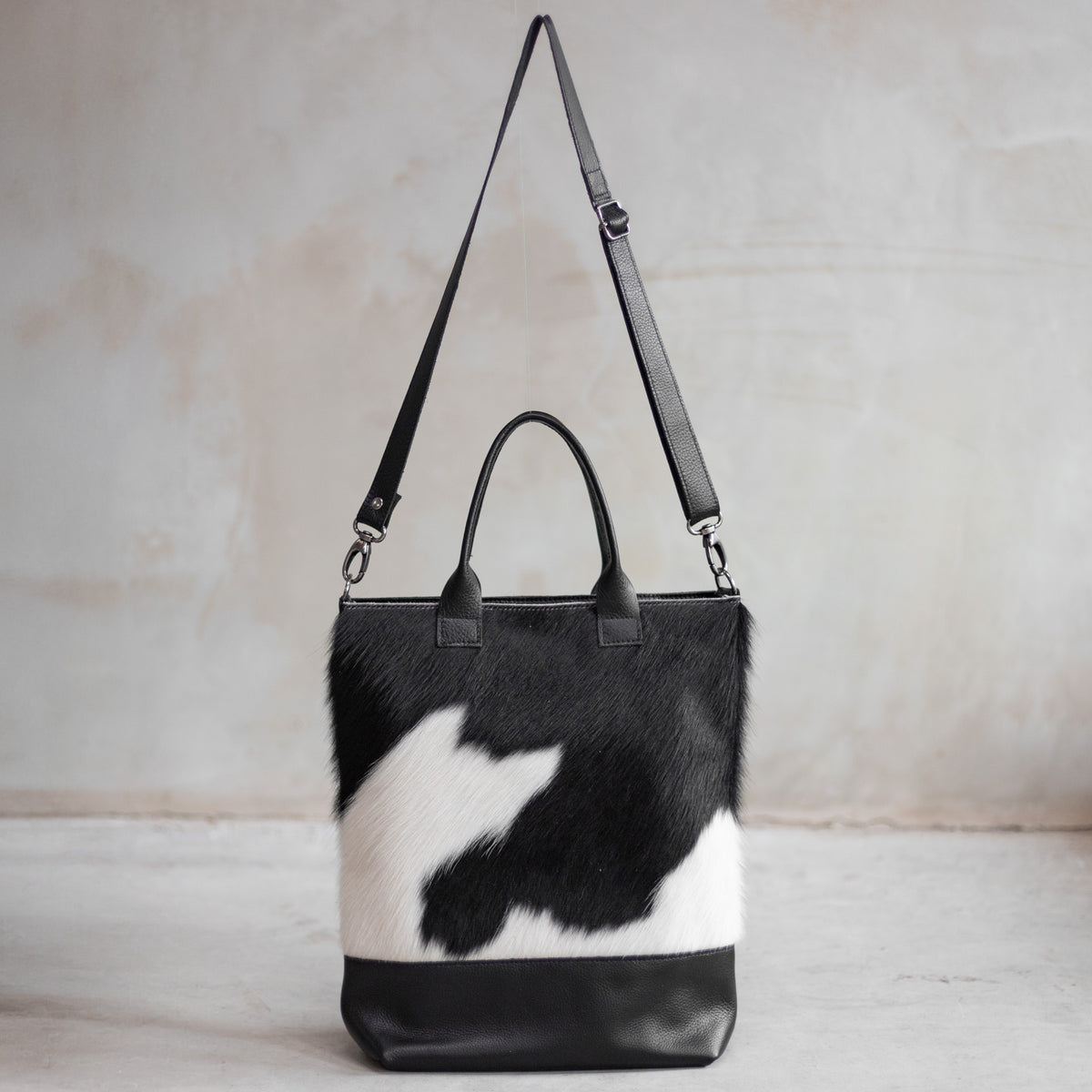 Grand sac à main en cuir et peau de vache noir et blanc, vu de face avec sa bandoulière en cuir noir