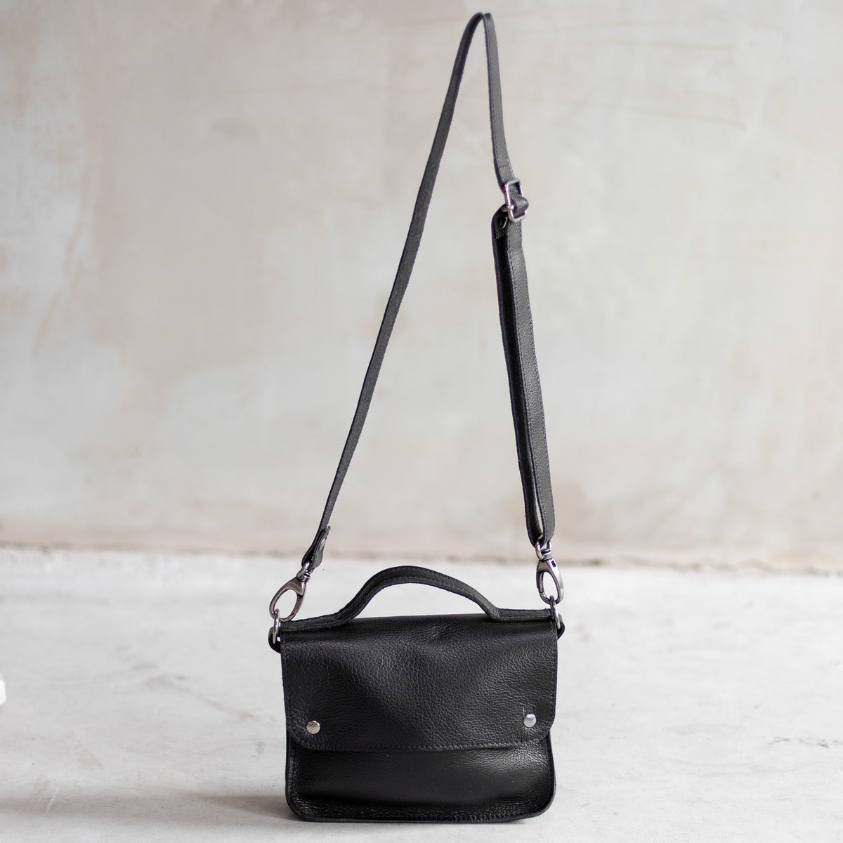 Petit sac à main bandoulière en cuir noir, vu de loin avec sa bandoulière