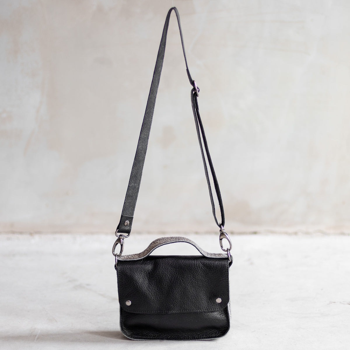 Petit sac à main bandoulière en cuir noir et côtés gris, vu de loin avec sa bandoulière