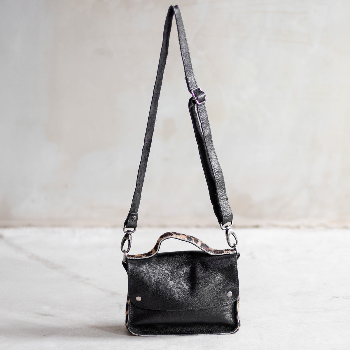 Petit sac à main bandoulière en cuir noir et côtés léopard, vu de loin avec sa bandoulière