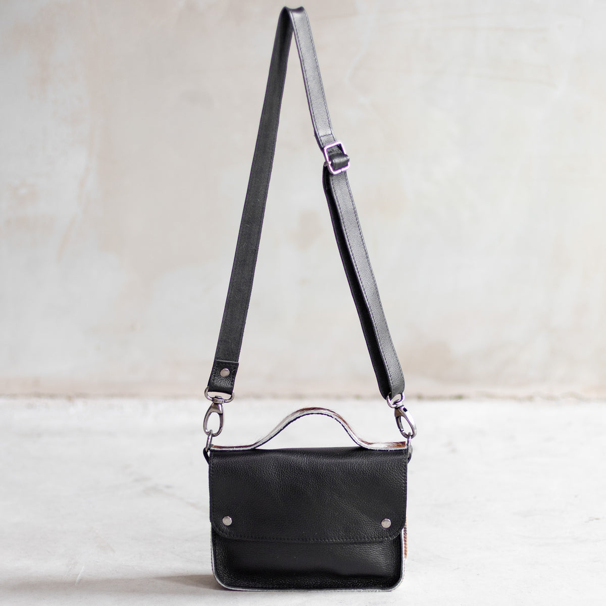 Petit sac à main bandoulière en cuir noir et côtés tricolores, vu de loin avec sa bandoulière