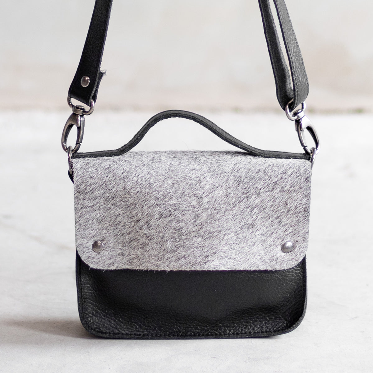 Petit sac à main bandoulière en cuir noir et rabat gris, vu de face, rabat en peau de vache grise