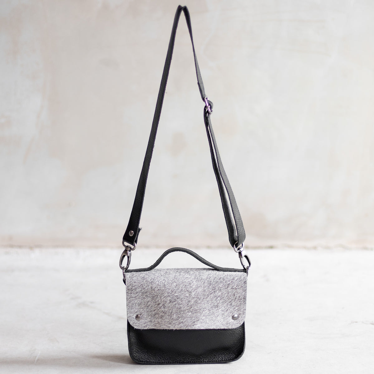 Petit sac à main bandoulière en cuir noir et rabat gris, vu de loin avec sa bandoulière