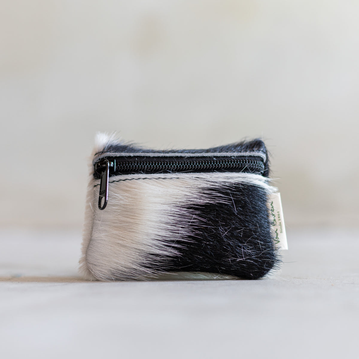 Porte-monnaie zippé en peau de vache noir et blanc, vu de face, fermeture éclair