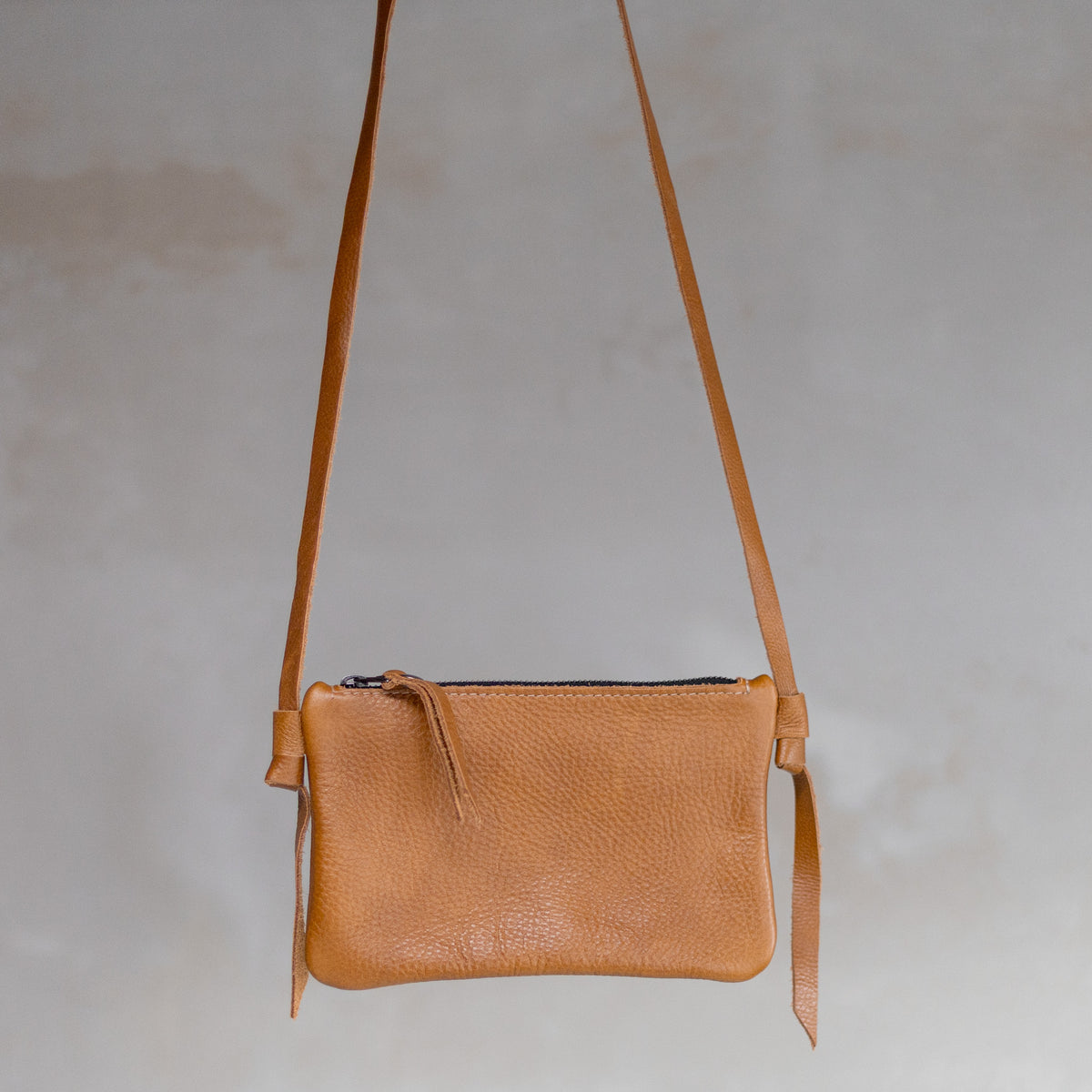 Sac à main pochette bandoulière en cuir cognac, suspendue par sa bandoulière