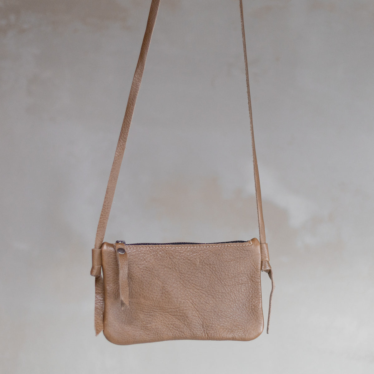 Sac à main pochette bandoulière en cuir sable, suspendue par sa bandoulière