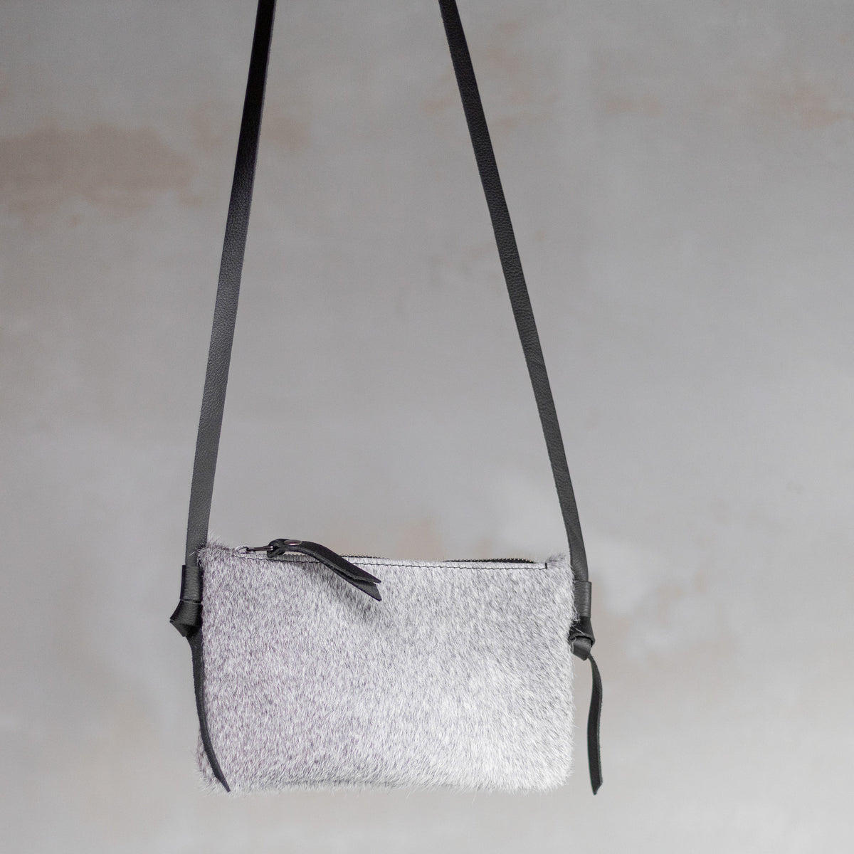 Sac à main pochette bandoulière en peau de vache grise, suspendue par sa bandoulière