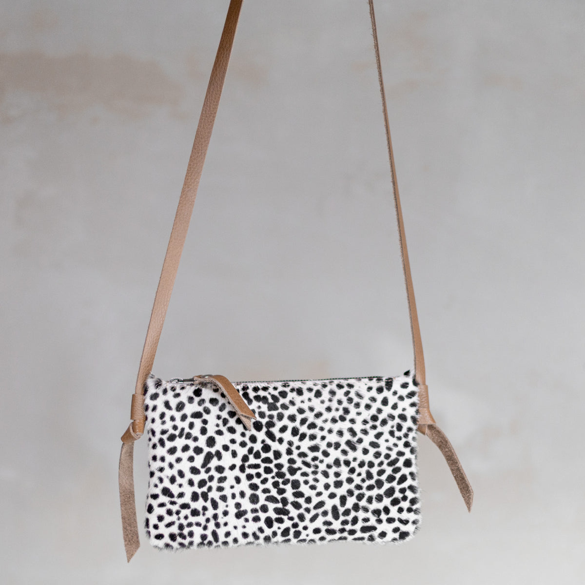 Sac à main pochette bandoulière en peau de vache mini dalmatien, suspendue par sa bandoulière en cuir