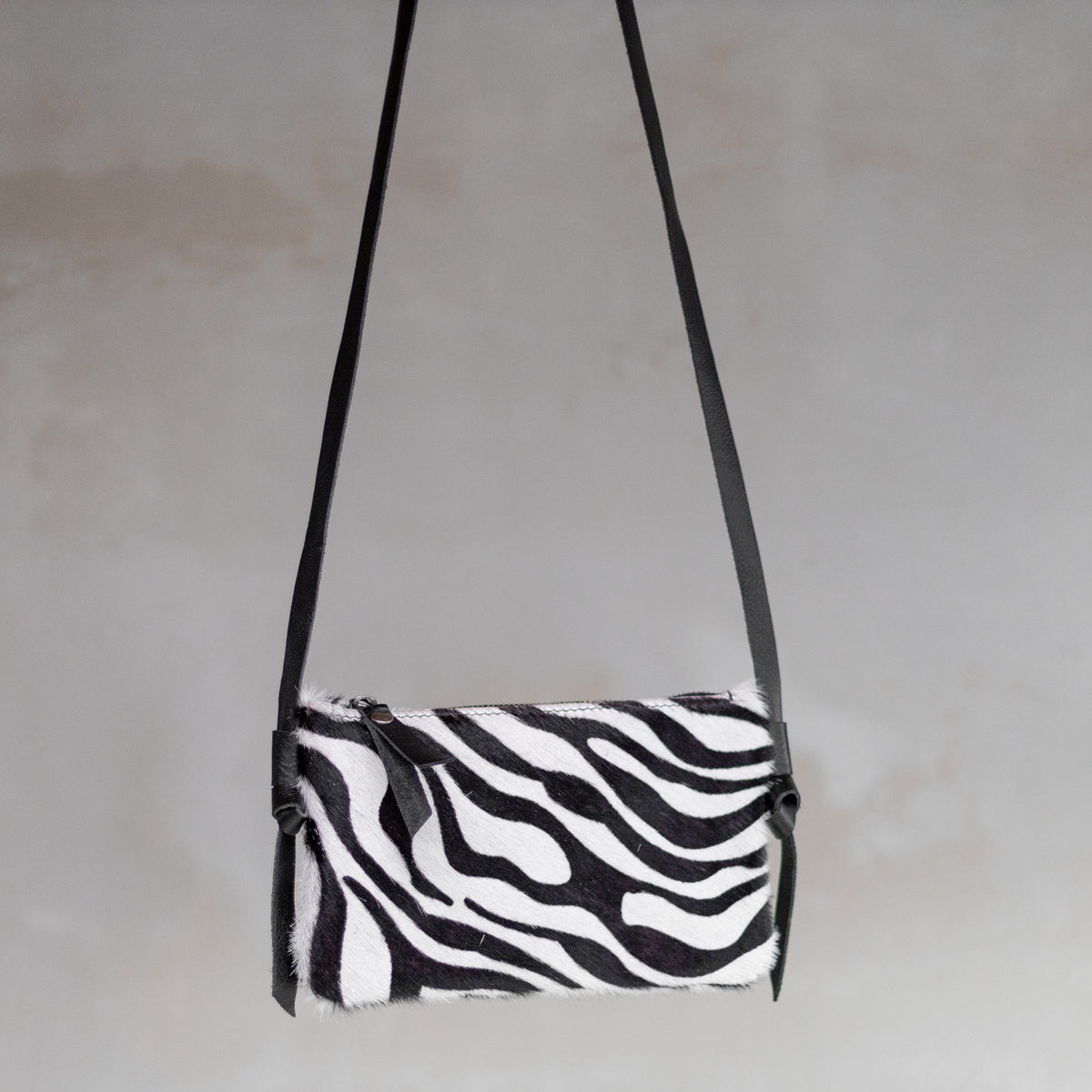 Sac à main pochette bandoulière en peau de vache zèbre, suspendue par sa bandoulière en cuir
