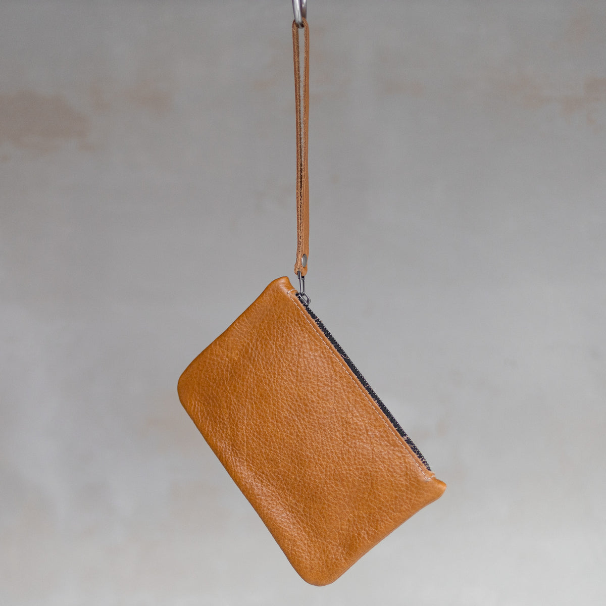 Sac à main pochette en cuir cognac, suspendue par sa dragonne