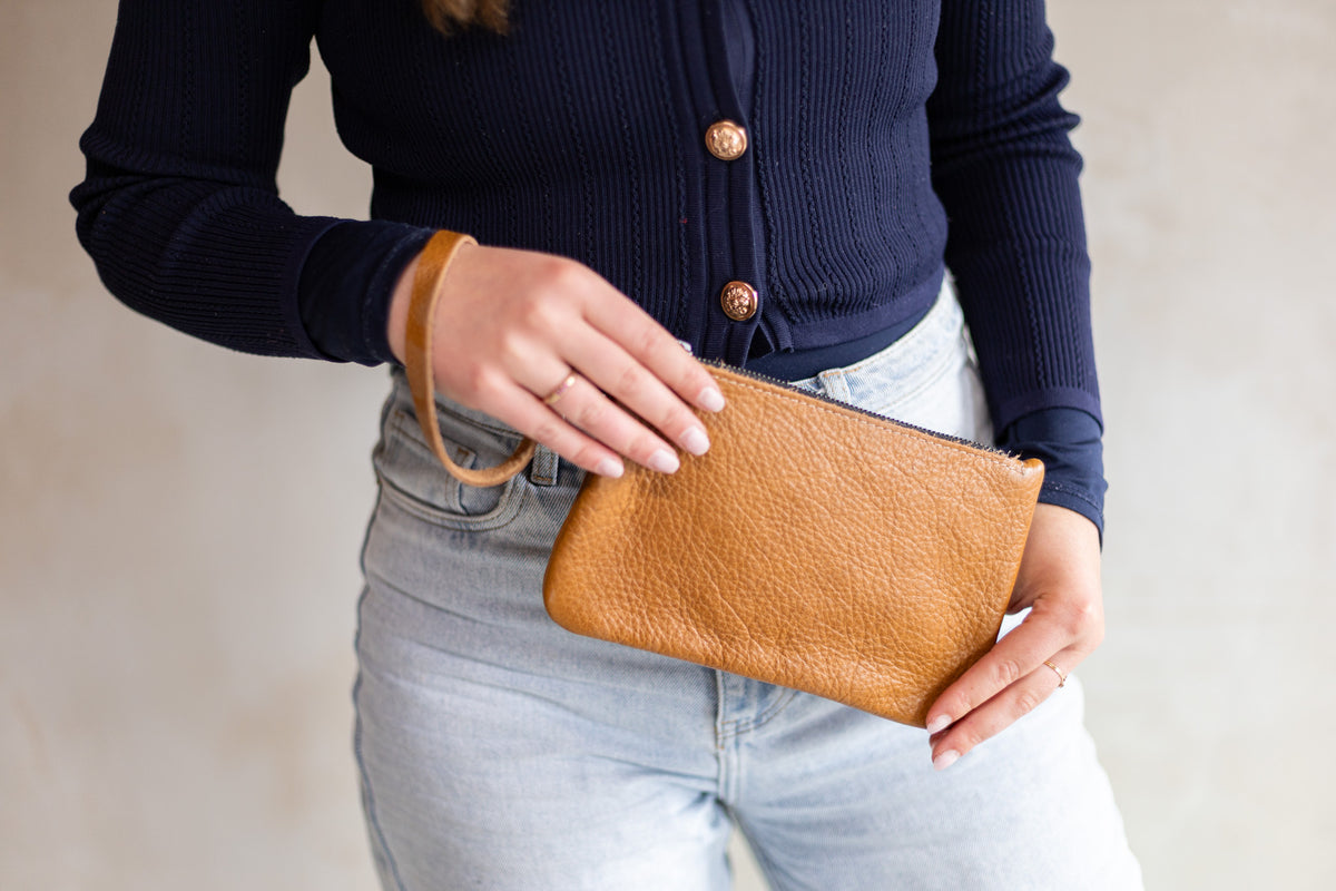 Sac à main pochette en cuir cognac, tenue à deux mains avec un jean