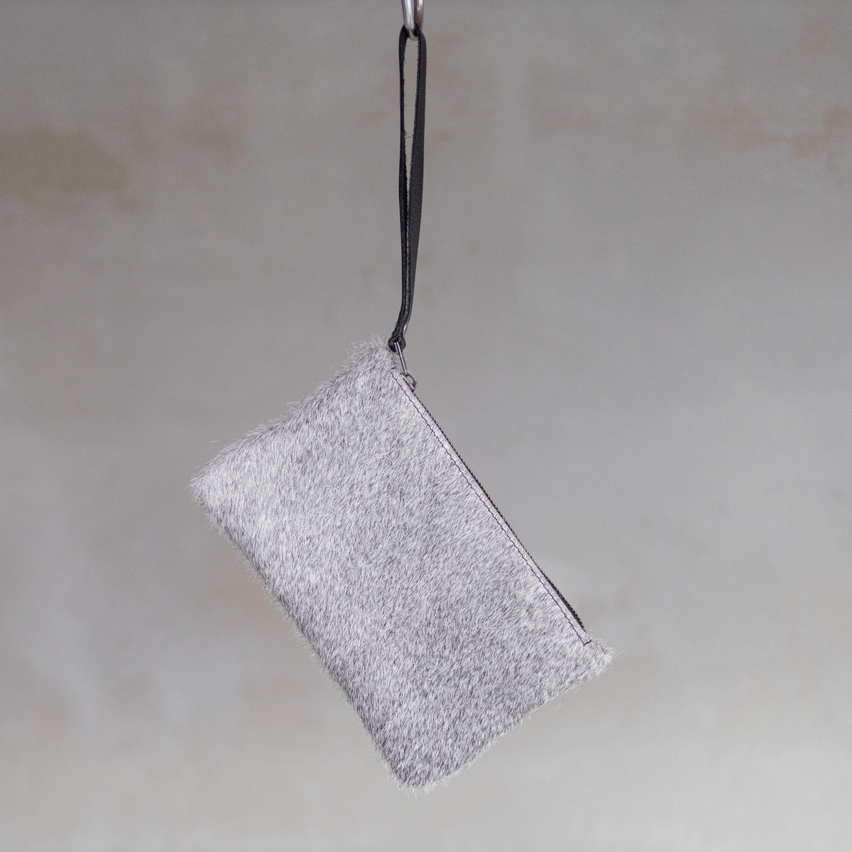 Sac à main pochette en peau de vache grise, suspendue par sa dragonne