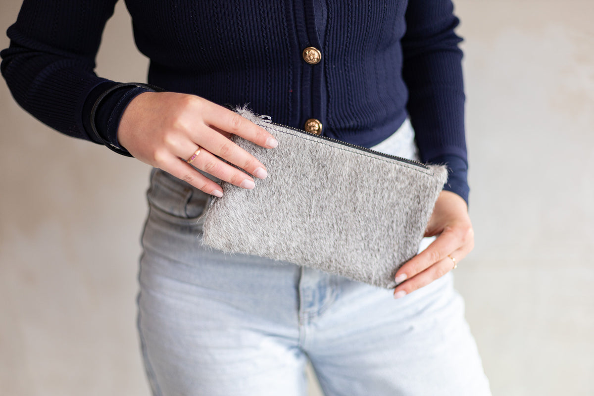 Sac à main pochette en peau de vache grise, tenue à deux mains avec un jean