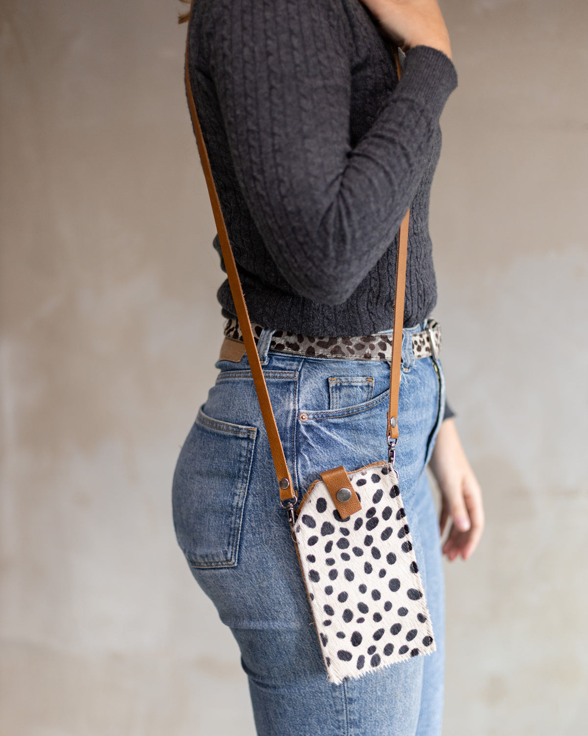 Sac à main pochette téléphone en peau de vache dalmatien, portée en bandoulière avec un jean