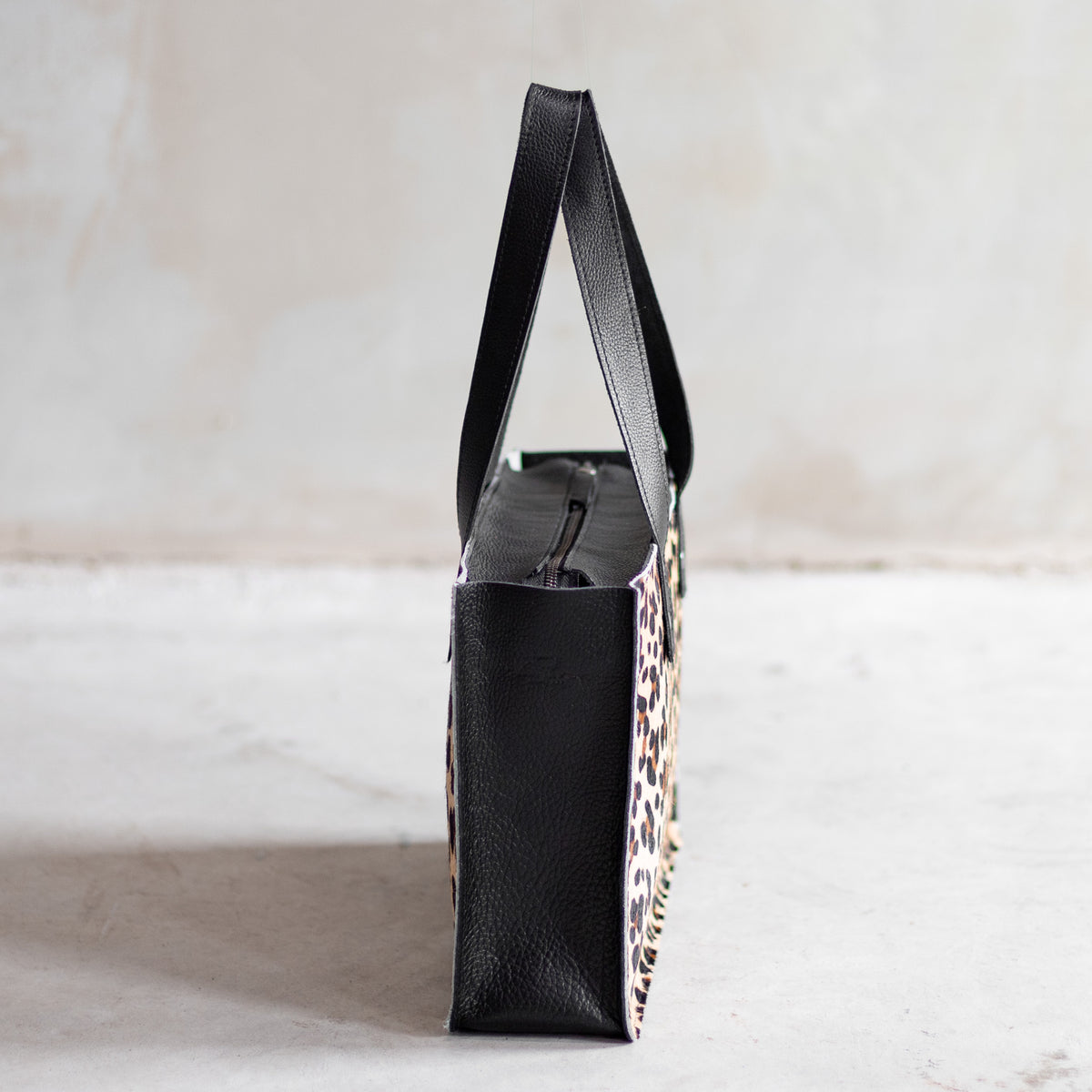 Sac à main rectangulaire en cuir noir et peau de vache léopard, vu de profil